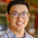 A man with black hair and glasses smiles at the camera
