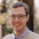 Brown haired man with glasses is smiling at the camera