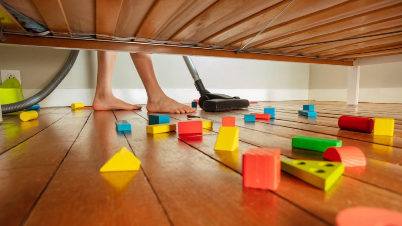 Photograph of someone vacuuming a wooden floor under a couch, with children's blocks on the floor