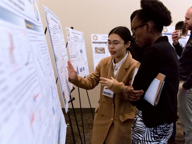 Two female students point and discuss over a research poster