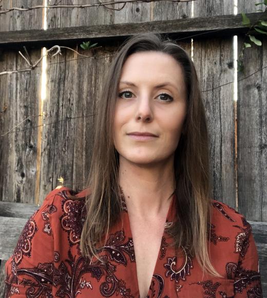 Woman with brown hair wearing red shirt with wooden fence in background