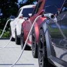 Electric cars charging at a station, with cables connected and greenery in the background.