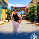 A person wearing a black top and white pants walks down a colorful, sunny street. Text in the bottom right corner says "Global Aggies".